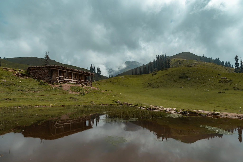 Brown house near green grass field and lake under cloudy sky